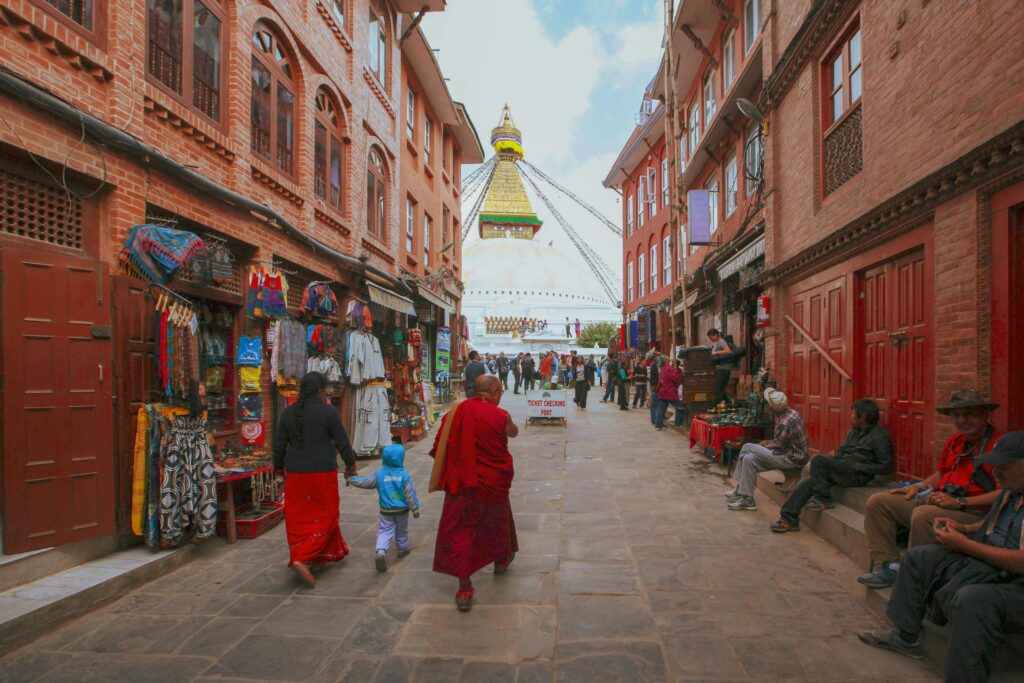 Monks and locals walk along a vibrant street near Boudhanath Stupa in Kathmandu, Nepal.