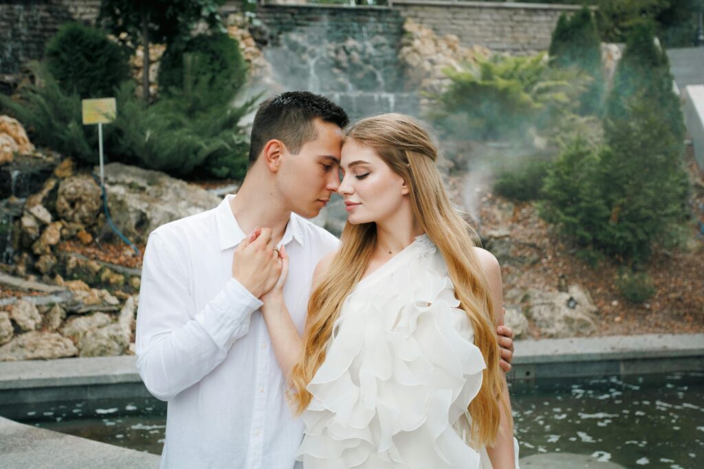 Young couple in a romantic embrace, standing near a garden pond in a tranquil outdoor setting.
