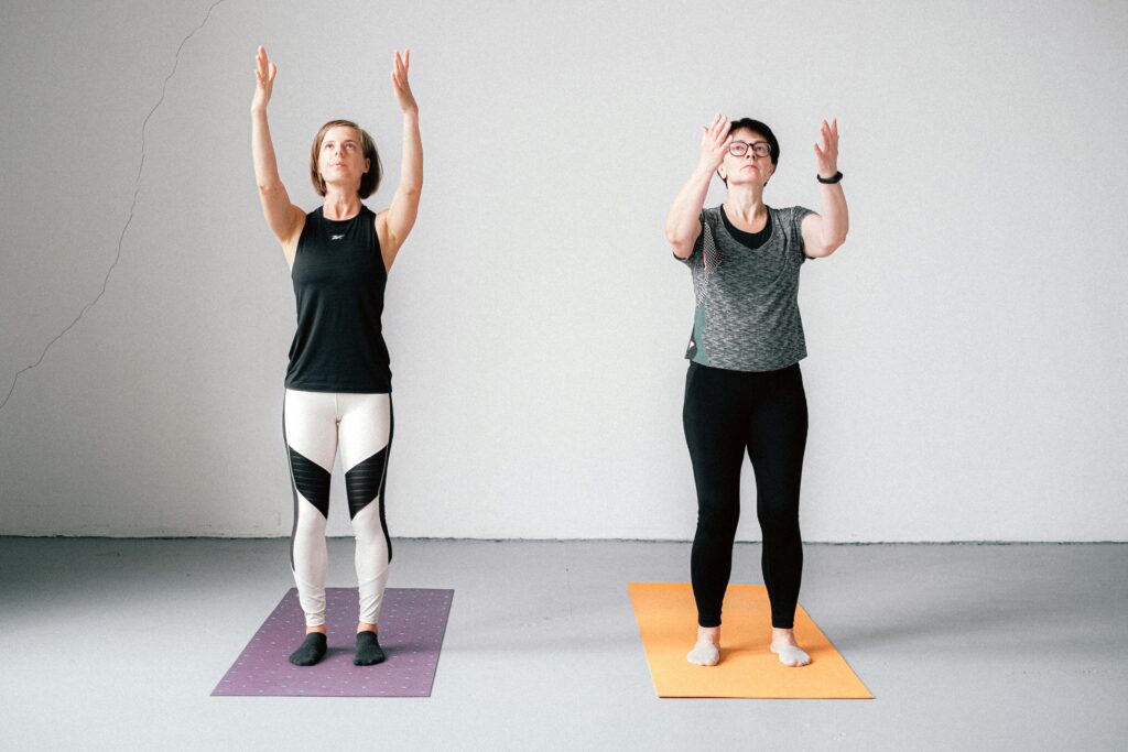 Two women practicing yoga indoors on mats, focused and relaxed, promoting fitness and well-being.