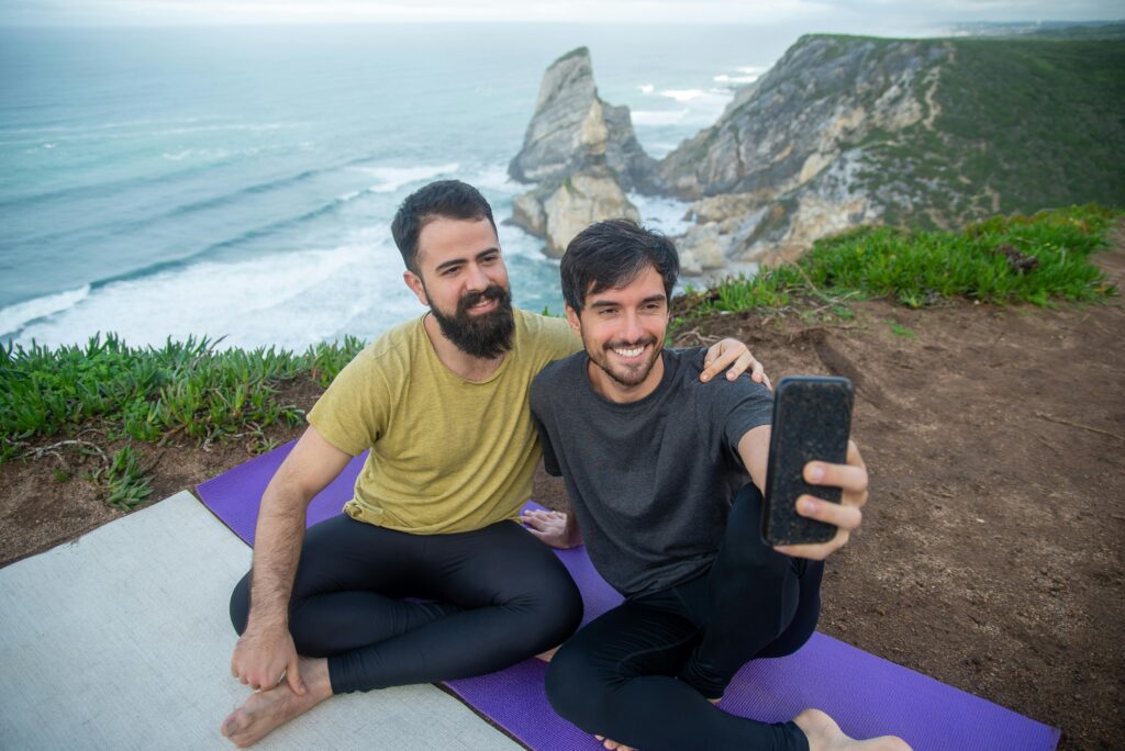 Smiling couple taking a selfie during yoga session on a coastal cliff in Portugal.
