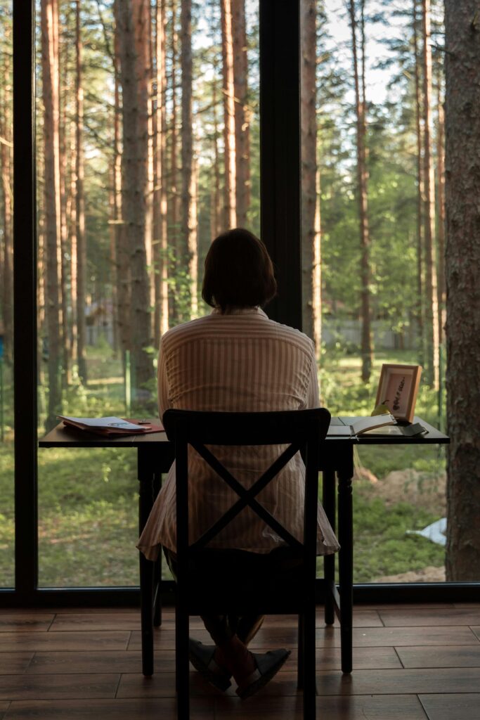 A person enjoys a peaceful work session by a forest view window.