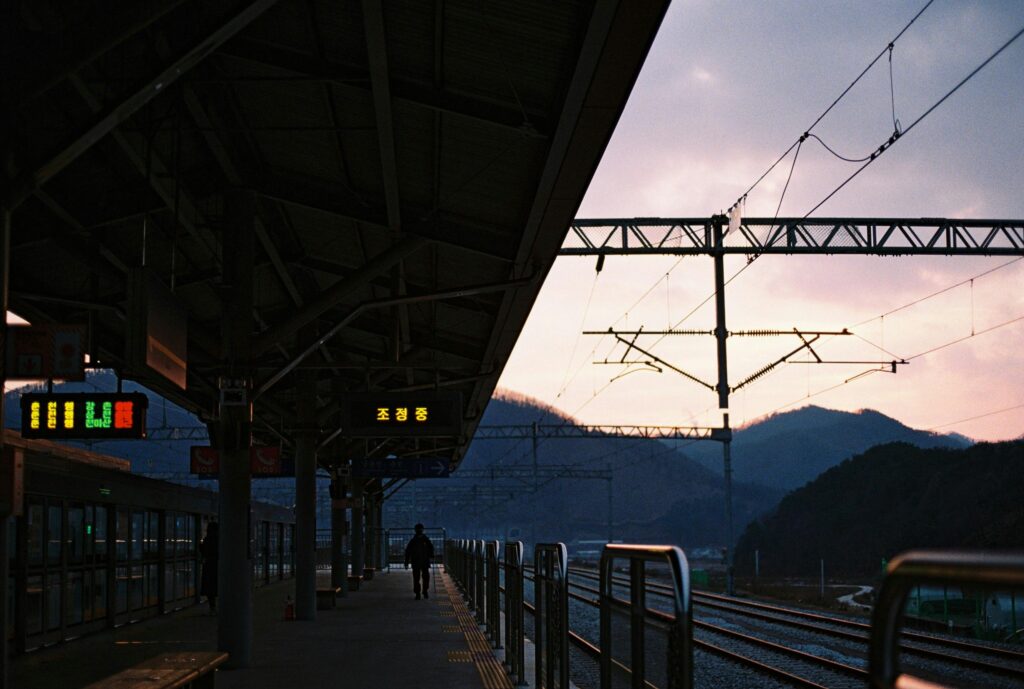 Dusk at a railway station with a silhouetted figure on the platform and colorful sky.