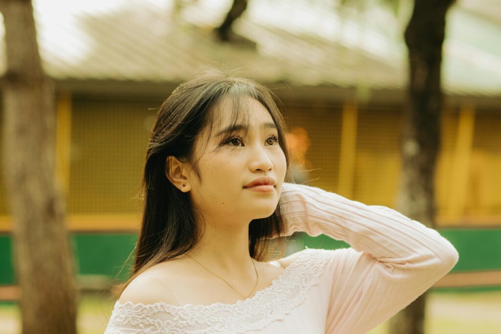 Beautiful young Asian woman gazing upward in a sunny park setting.