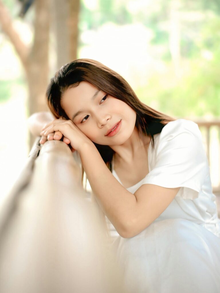 Serene portrait of a woman in white resting outdoors with a thoughtful expression.