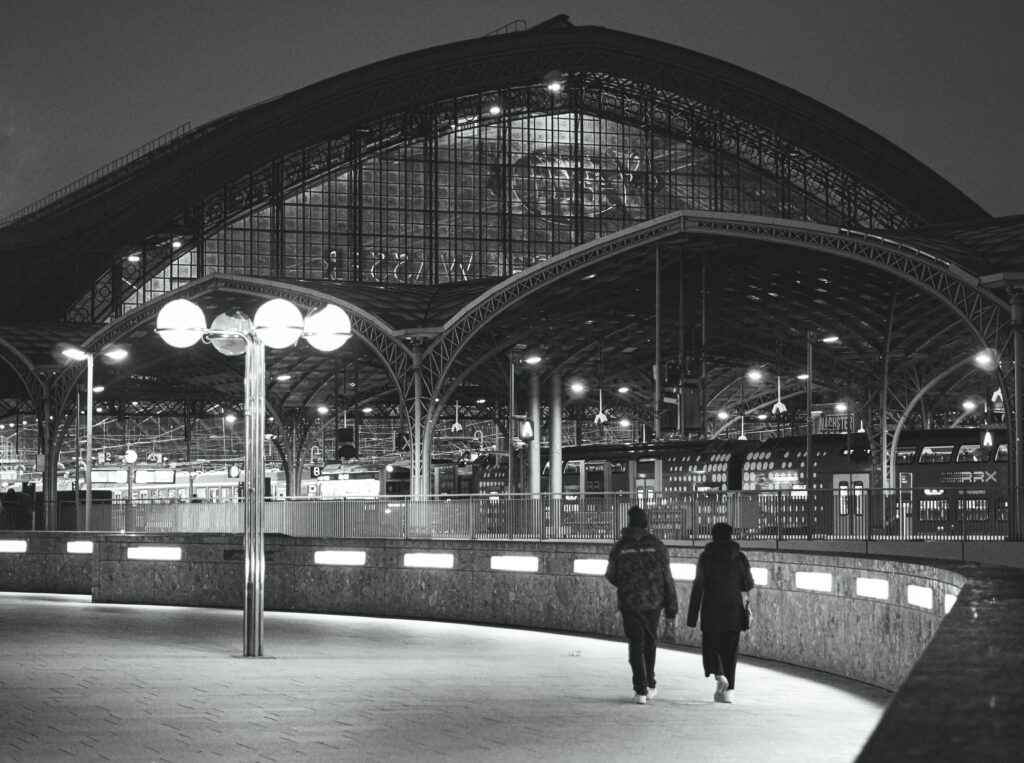 Two people walking towards Cologne Central Station at night, showcasing architectural beauty.