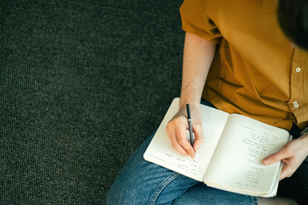 Close-up of a person taking notes in a notebook while sitting on the floor, emphasizing education and focus.