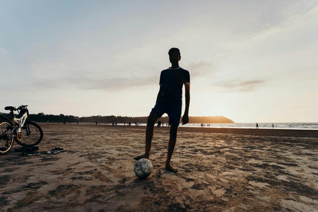 Silhouette of a man on a sandy beach with a soccer ball at sunset, showcasing leisure and recreation.