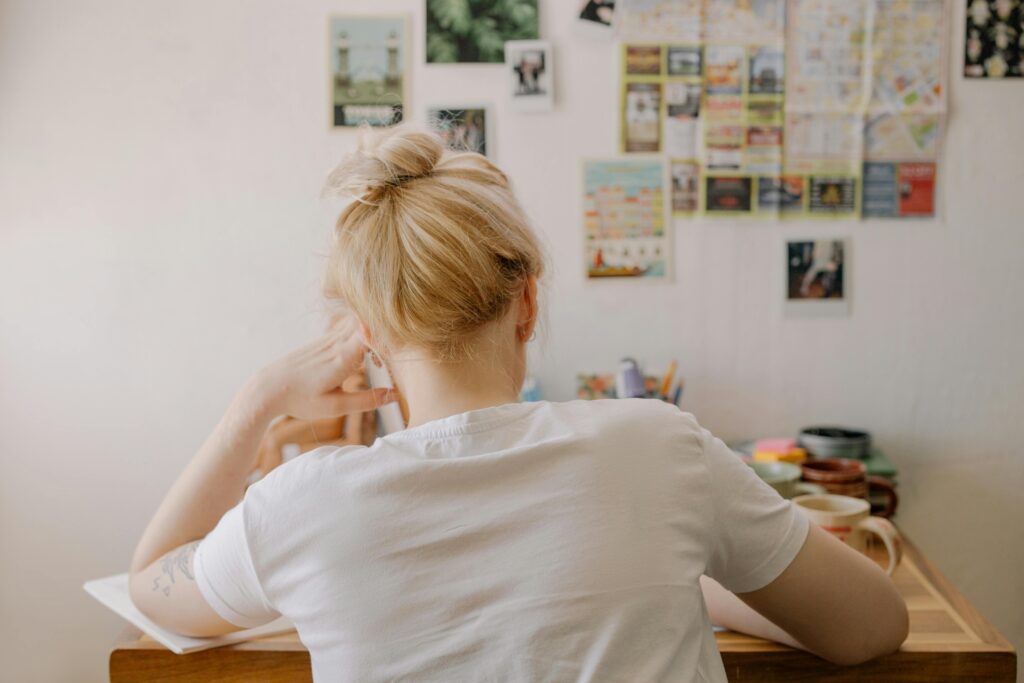 A woman with a blonde bun concentrates on study at a desk filled with study materials.