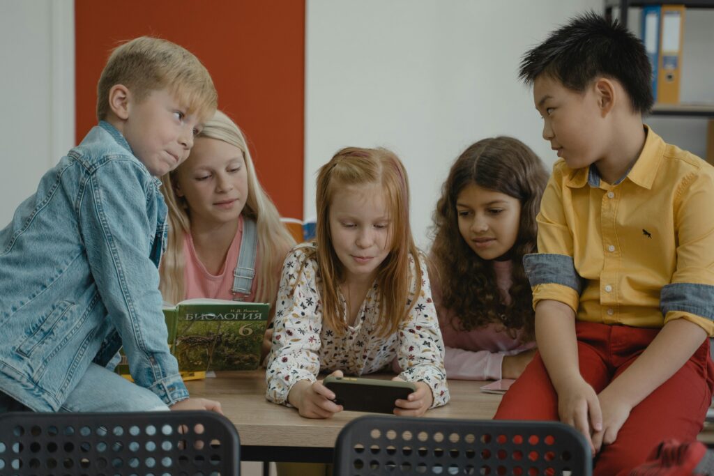 Children in a classroom using a smartphone for educational purposes, showcasing diversity and teamwork.