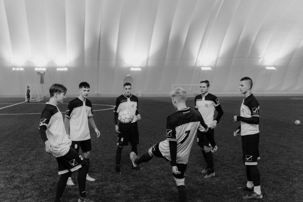 A group of male soccer players practicing indoors on an artificial field in monochrome.
