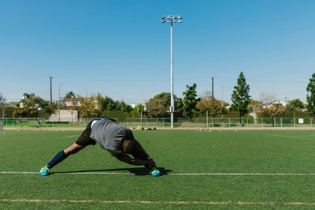 Athlete stretching on a soccer field during a sunny day, preparing for a workout.