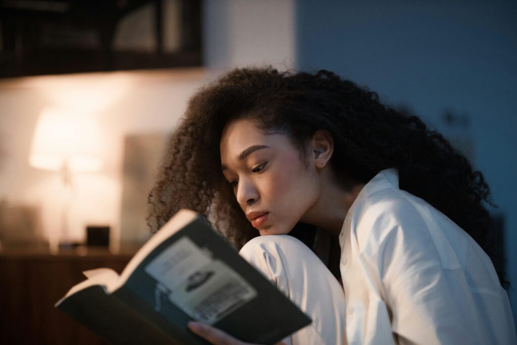A woman with curly hair enjoys reading a book indoors, creating a cozy and relaxed atmosphere.
