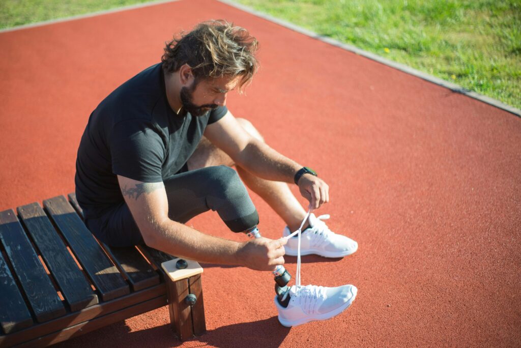 Adult male athlete with a prosthetic leg tying shoes on an outdoor track.