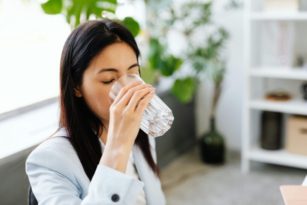 Adult woman sipping water from a glass in a modern office setting.