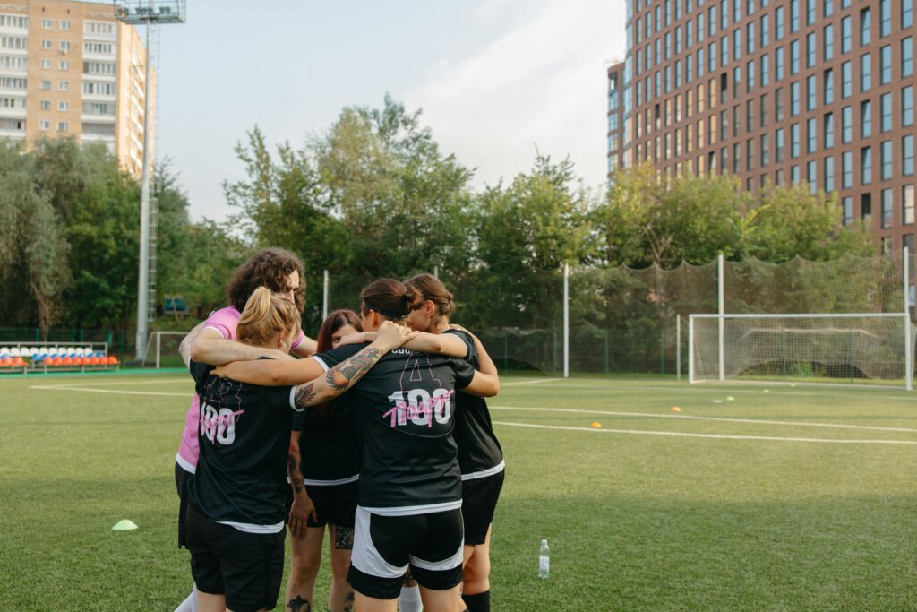 Women's football team huddles on a city field, emphasizing teamwork and sportsmanship.